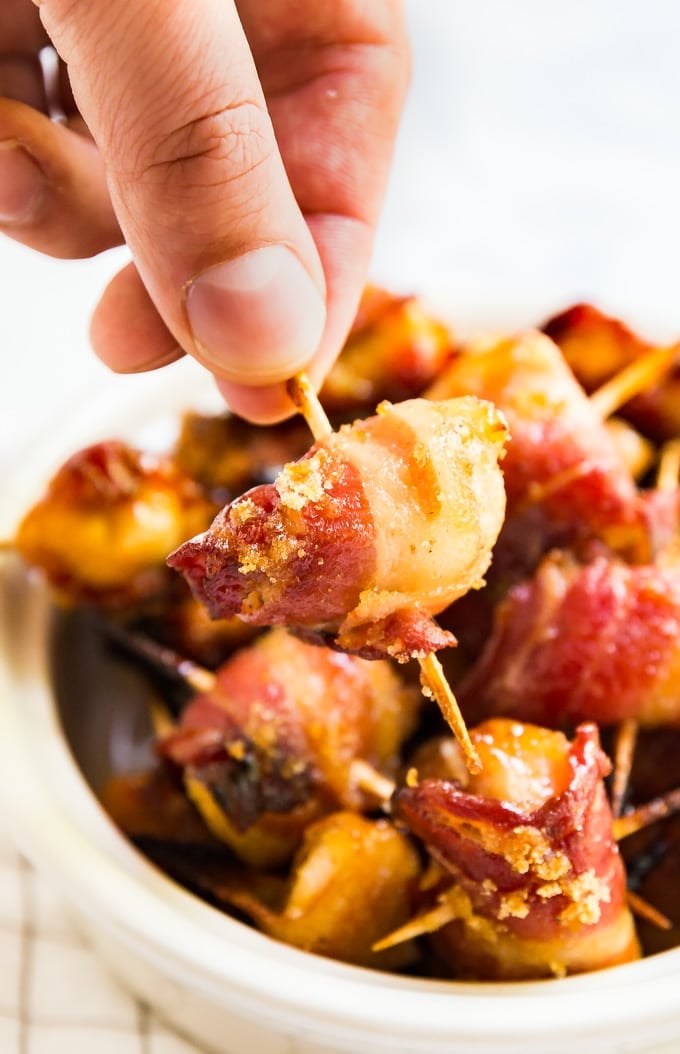 Hand picking up a Bacon Wrapped Chicken Bite using a toothpick
