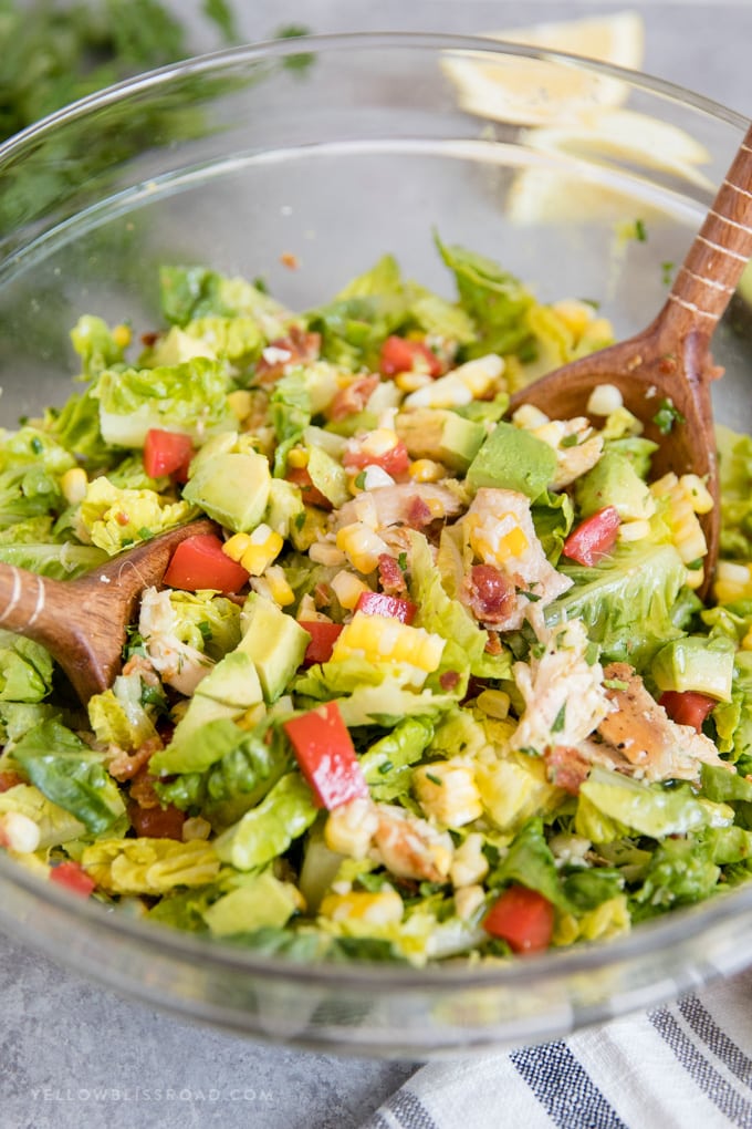 Bacon Avocado Chicken Salad with Lemon Vinaigrette being tossed in a bowl with wooden salad spoons.