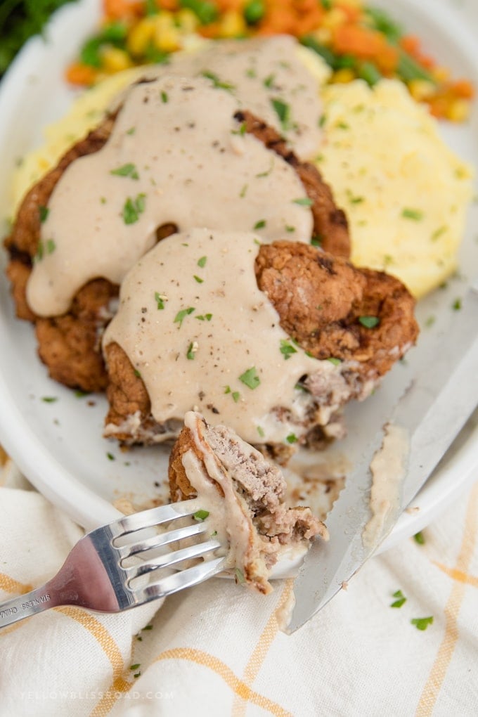 chicken fried steak with homemade gravy on mashed potatoes with one piece on a fork.