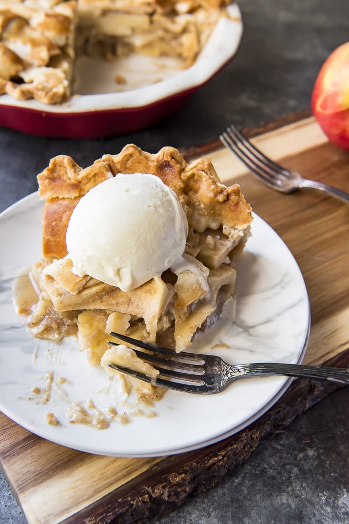 A flaky, delicious Classic Apple Pie Recipe is perfect for dessert all year round! Slightly crunchy cinnamon & caramel-coated apples are tucked into a homemade pie crust and baked into the prettiest dessert on the block! Classic Apple Pie slice topping with ice cream