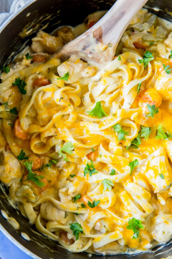 An overhead shot of a pan of creamy chicken and noodles with a wooden spoon