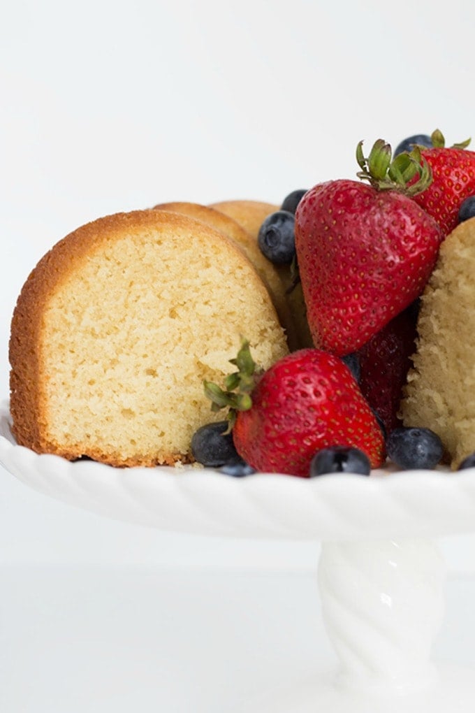 This soft, buttery Pound Cake Recipe is perfect by itself or topped with fresh fruit. It bakes up great in a bundt pan or loaf pan too! pound cake on a cake stand with a slice taken out