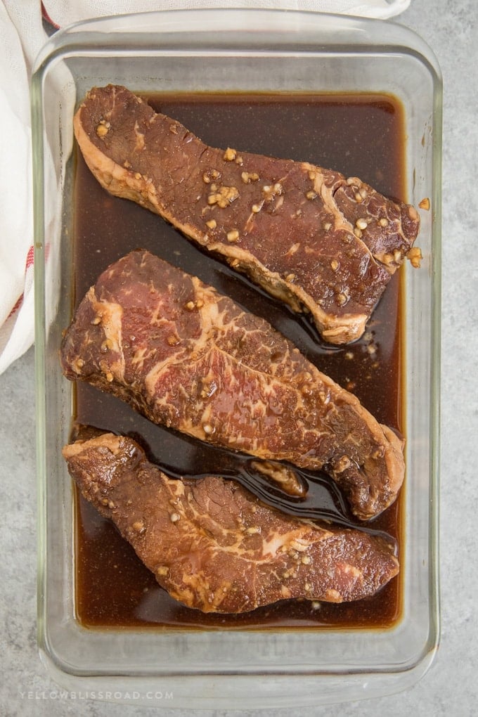 three strip steaks in a steak marinade
