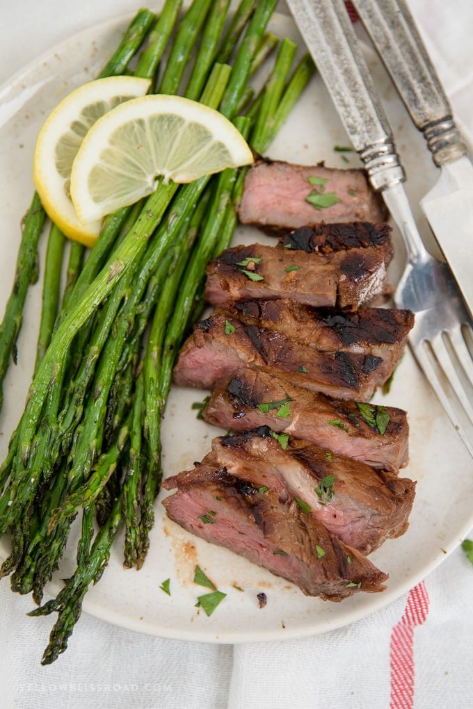 This Steak Marinade is super simple and packed with flavor, giving you a tender, juicy piece of meat every time you're grilling steak. grilled steak in steak marinade, sliced on a plate with some asparagus, plus guide for grilling steak.