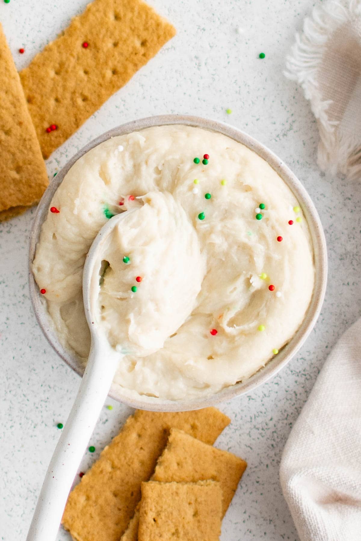 Sugar cookie dip in a small bowl with a spoon, surrounded by graham crackers.