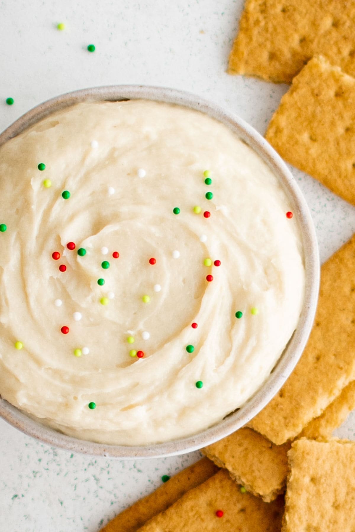 Sugar cookie dip in a bowl with sprinkles on top and surrounded by graham crackers. 