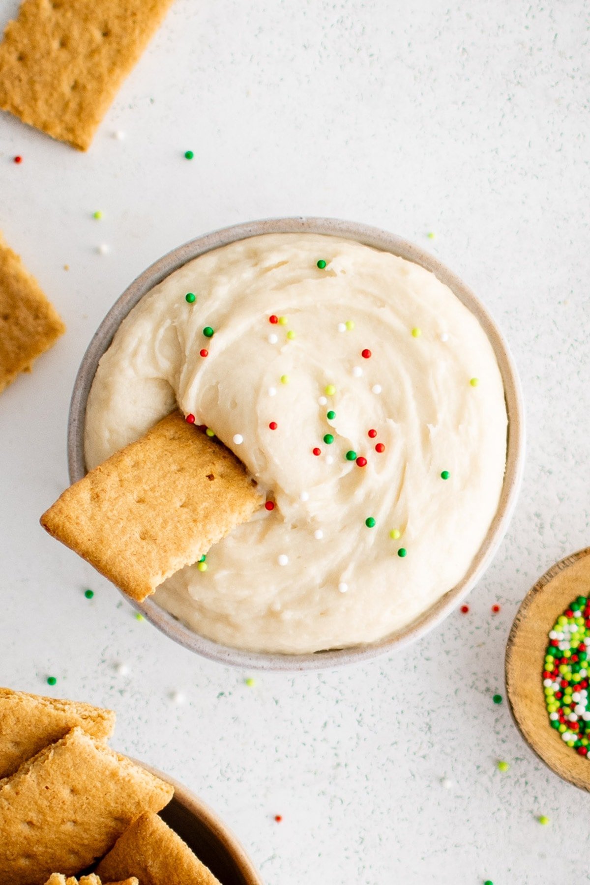 Sugar cookie dip in a bowl with a graham cracker and sprinkles.