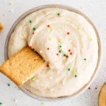 Sugar cookie dip with a graham cracker dipped in and sprinkles.
