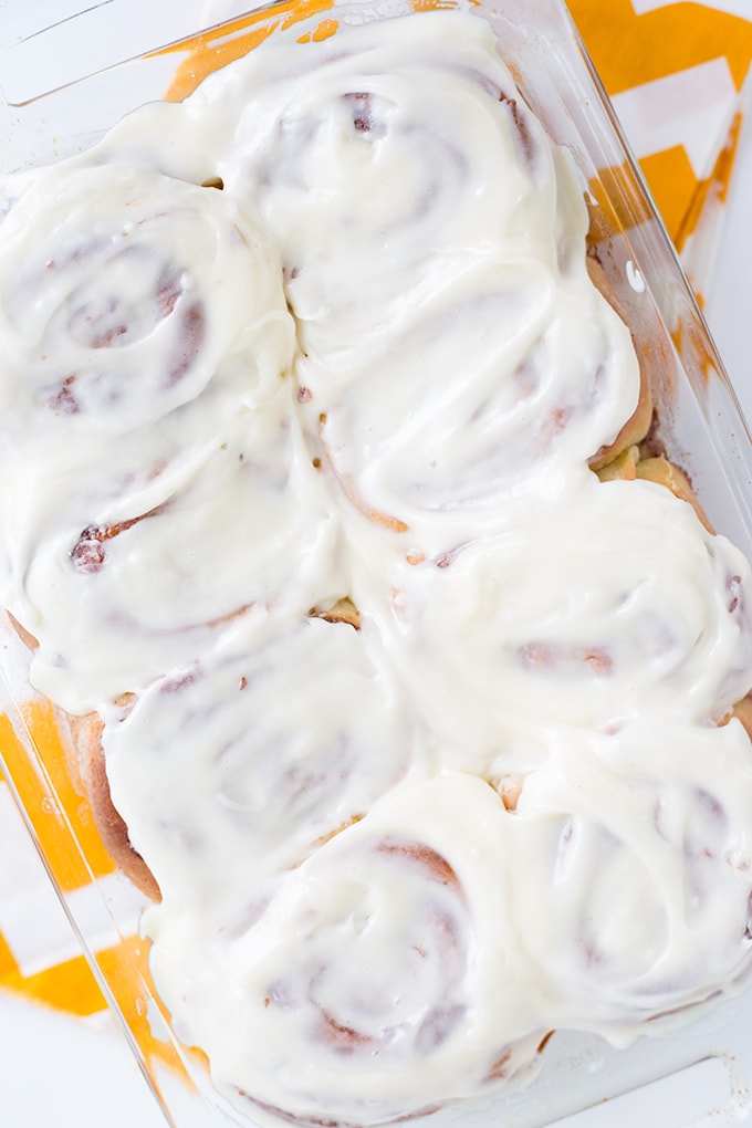 homemade cinnamon rolls in a baking dish covered in cream cheese frosting