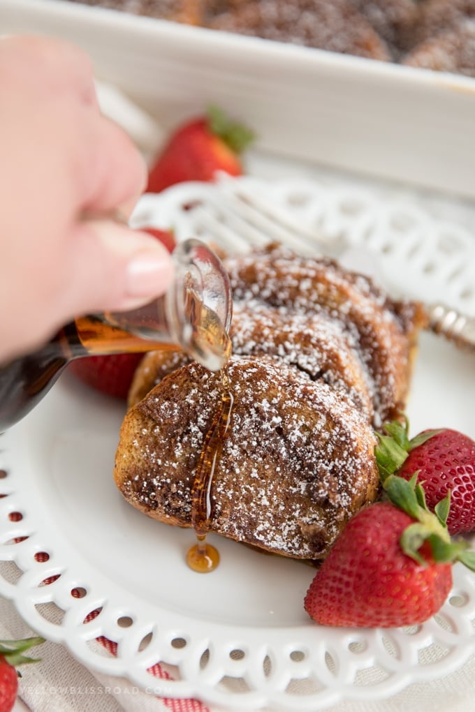 slices of overnight baked french toast with powdered sugar with syrup poured on top.