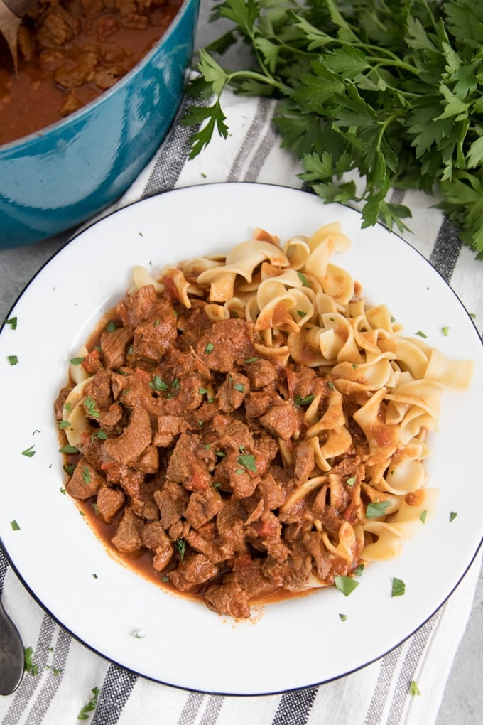 Hungarian goulash served on a plate over egg noodles.