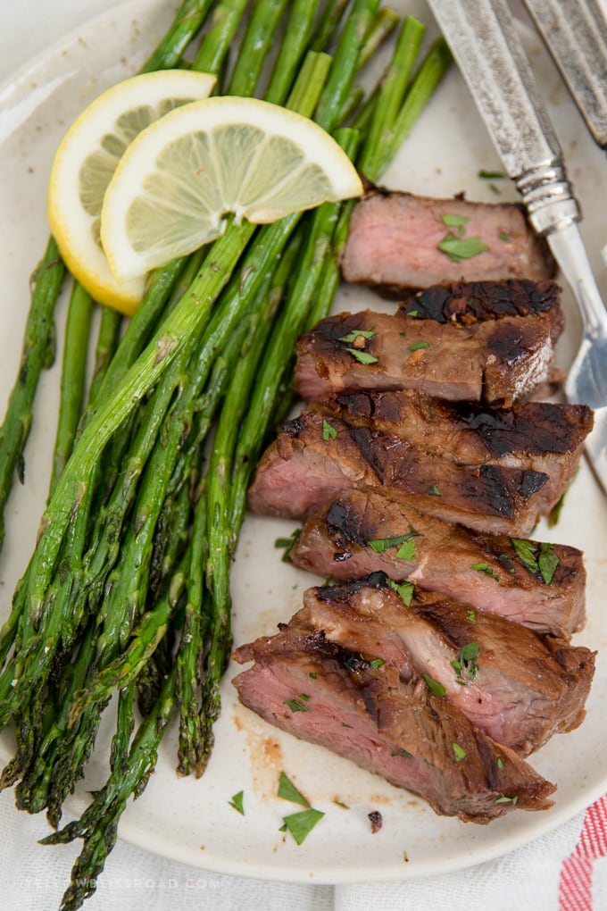 Oven roasted asparagus on a plate with sliced pieces of grilled steak.