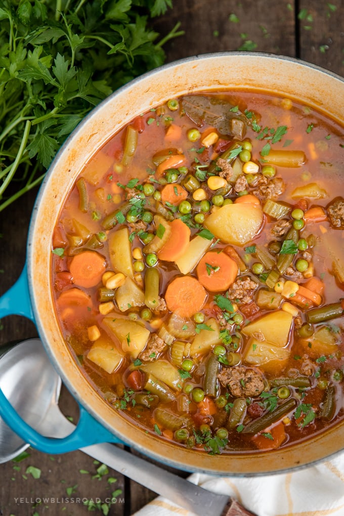 Smoky Vegetable Beef Soup is a simple dinner made in one pot, with a tomato beef broth, ground beef and tons of vegetables. A large blue pot with Smoky Vegetable Beef Soup in it.