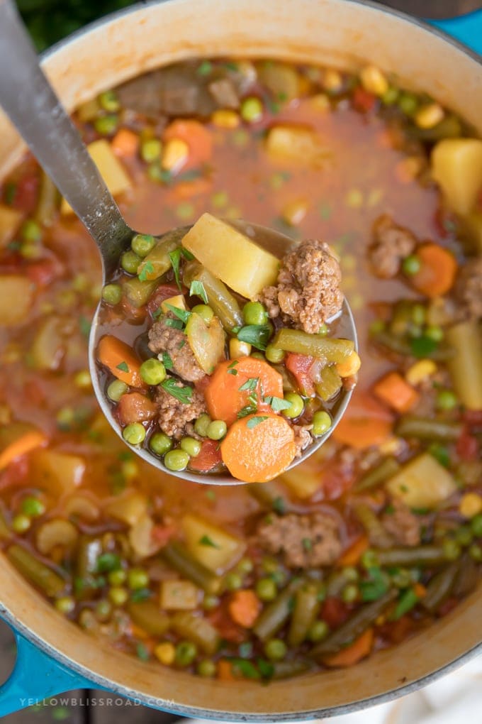 A ladle holding a scoop of vegetable beef soup over a large pot.