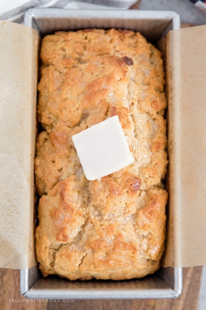 A loaf of beer bread in a loaf pan with a pat of butter.