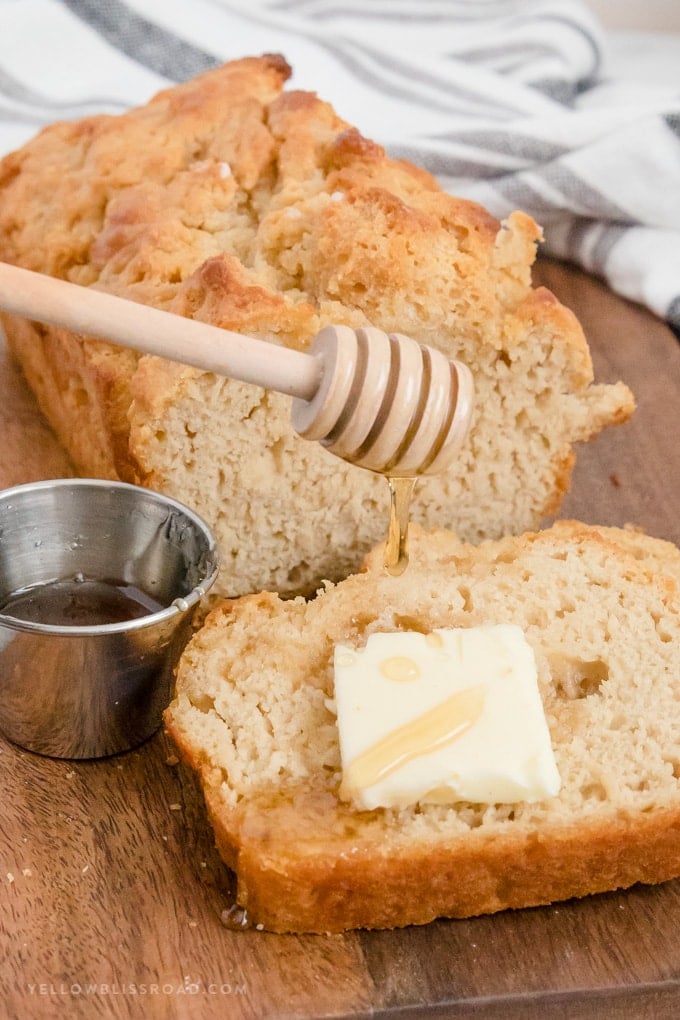 Beer bread loaf, a pat of butter and honey being drizzled on a slice.