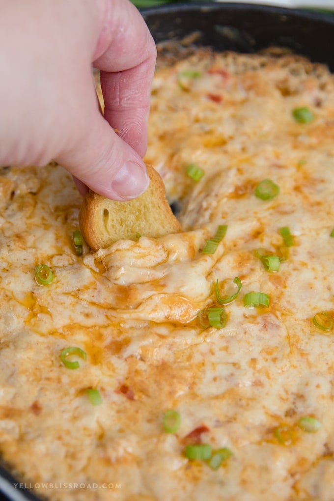 A piece of toasted bread dipped into a shrimp dip in a cast iron skillet.