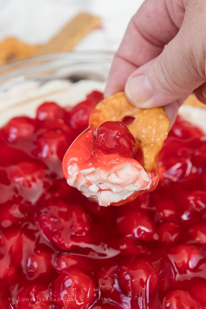 No Bake Cherry Cheesecake Dip is a yummy dessert for any occasion. Made with a sweet cream cheese base and cherry pie topping. Cherry Cheesecake Dip on a pretzel
