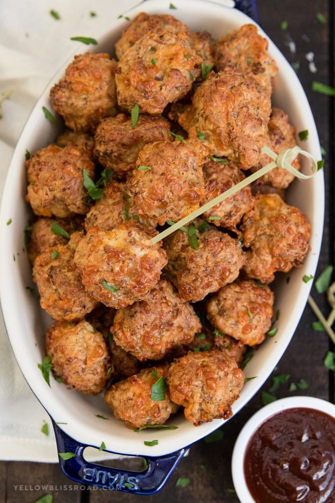 Cream Cheese Sausage Balls (Bisquick Sausage Balls) with a toothpick in a serving dish with a small dish of barbecue sauce.