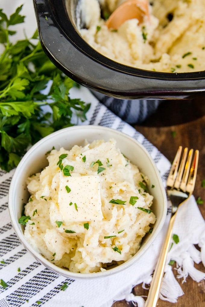 Crock Pot Mashed Potatoes | Slow cooker mashed potatoes in a bowl with a pat of butter and a gold fork.
