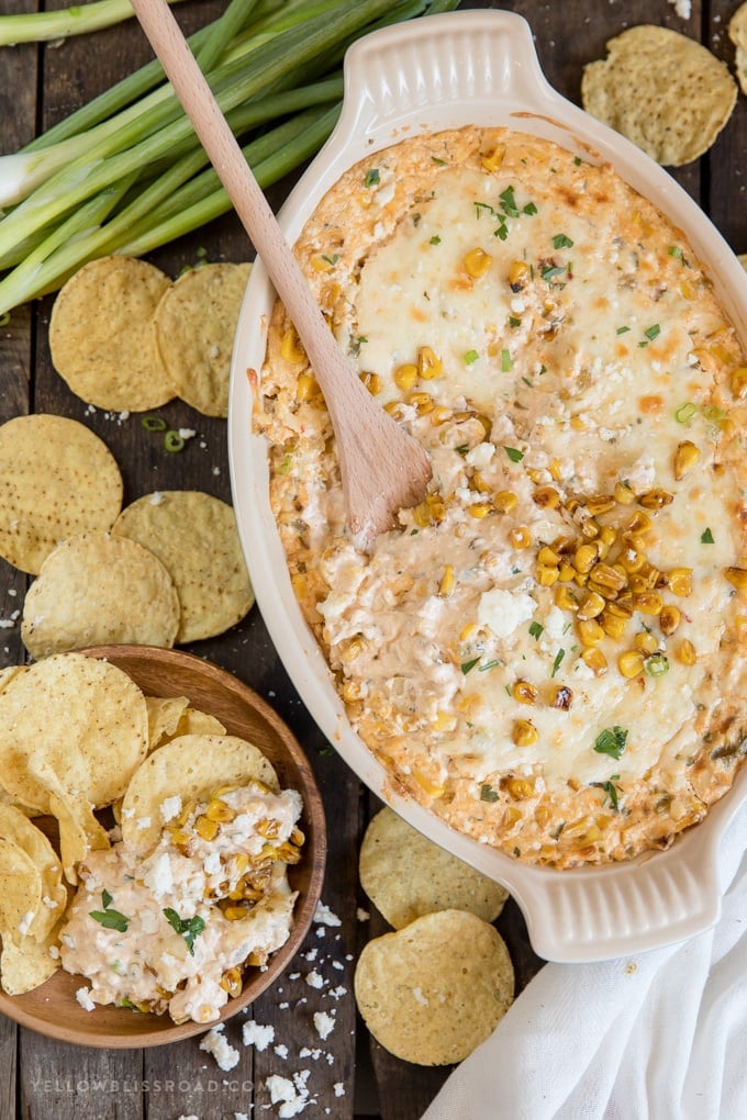 Ceramic baking dish, cheesy mexican corn dip, green onions, wooden spoon, tortilla chips, wood plate
