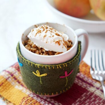 microwave apple crisp in a mug with whipped cream on top