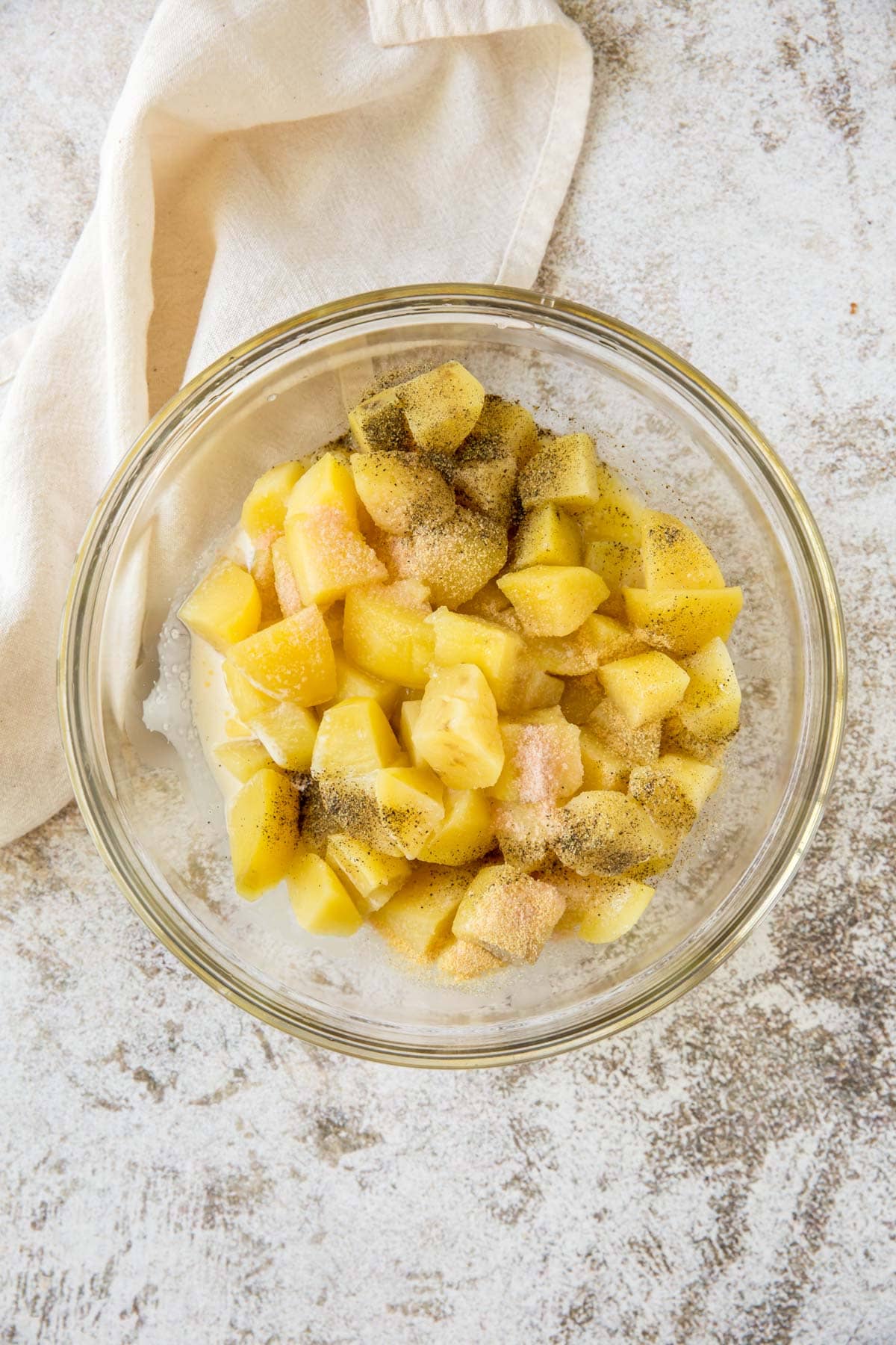 clear glass bowl with diced cooked potatoes, salt and pepper, a white napkin