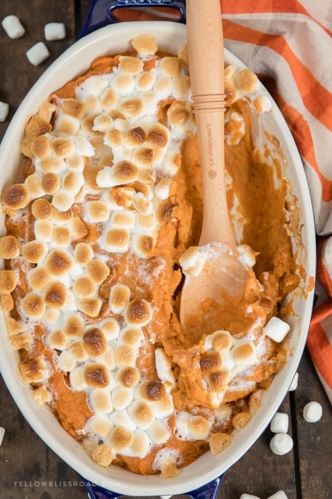 Sweet potato casserole with marshmallows and a wooden spoon.