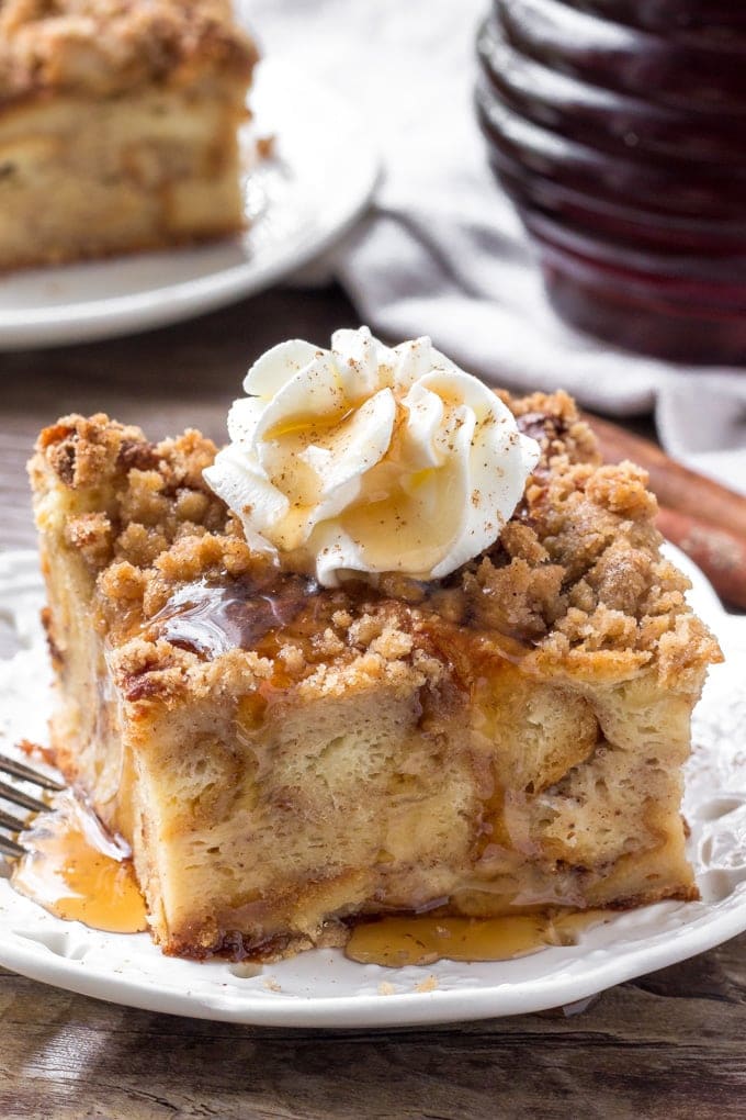 A close up shot of a slice of cinnamon french toast bake with whipped cream and syrup.