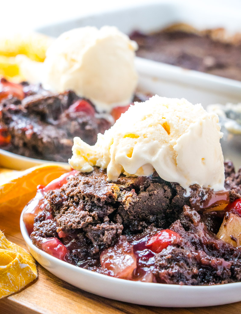 A couple servings of chocolate cherry dump cake on white plates with ice cream on top.