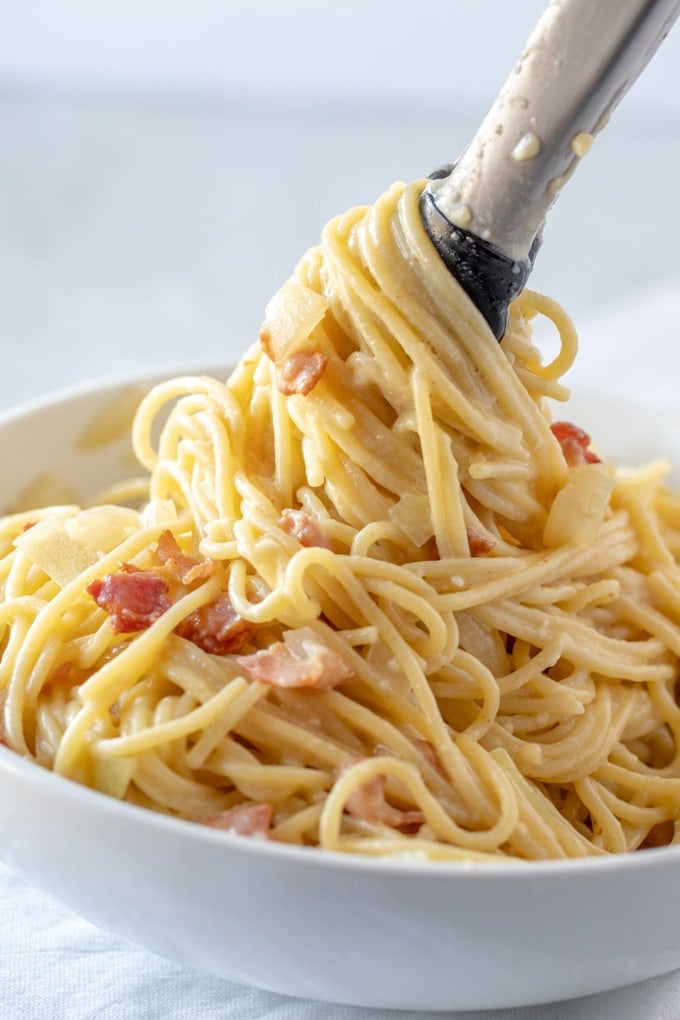 Pasta carbonara in a bowl with tongs twirling the spaghetti.