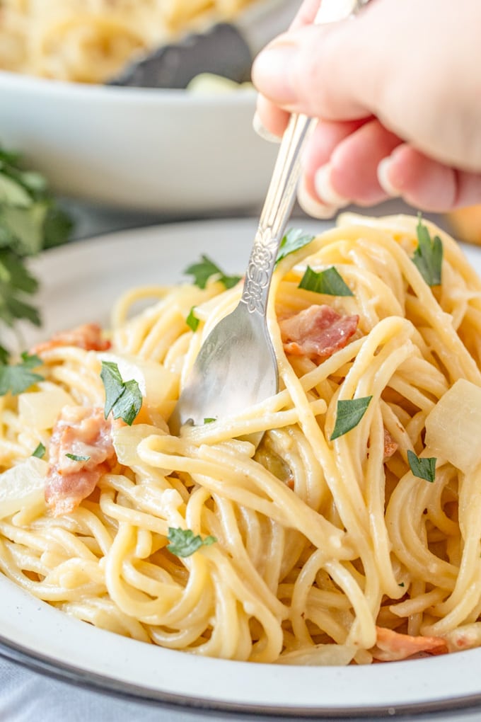 Authentic Pasta Carbonara recipe is a simple pasta dish in a cheesy egg sauce with lots of bacon and fresh ground black pepper. It's easy, yet elegant! A fork in a plate of pasta carbonara.