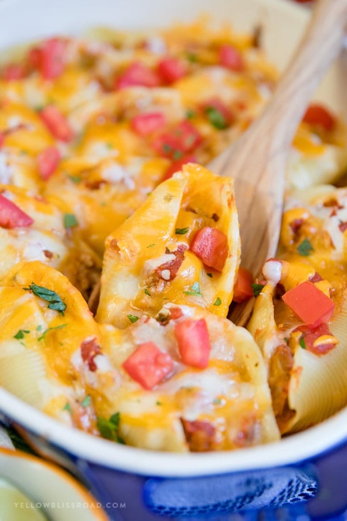 A pan of ground turkey taco stuffed shells with a wooden spoon.