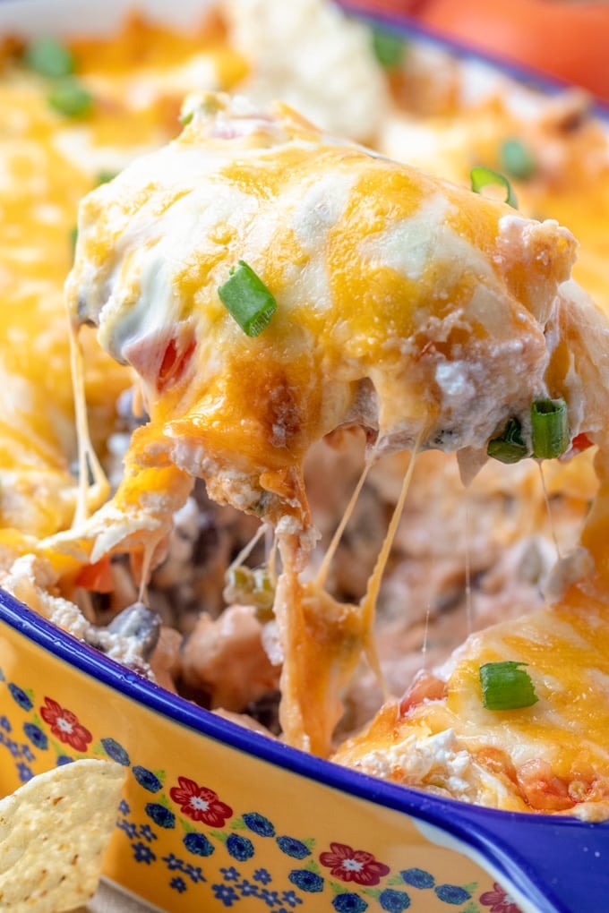 yellow casserole dish with blue and red flowers, creamy chicken casserole, melted cheese, tomatoes, black beans, green onions