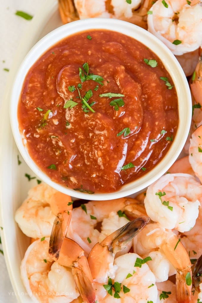 A bowl of homemade cocktail sauce surrounded by a platter of shrimp.