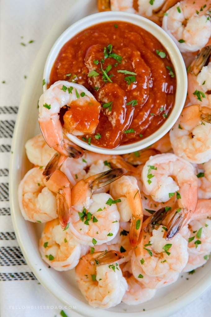 A shrimp dipped in homemade cocktail sauce sitting on the edge of the bowl.