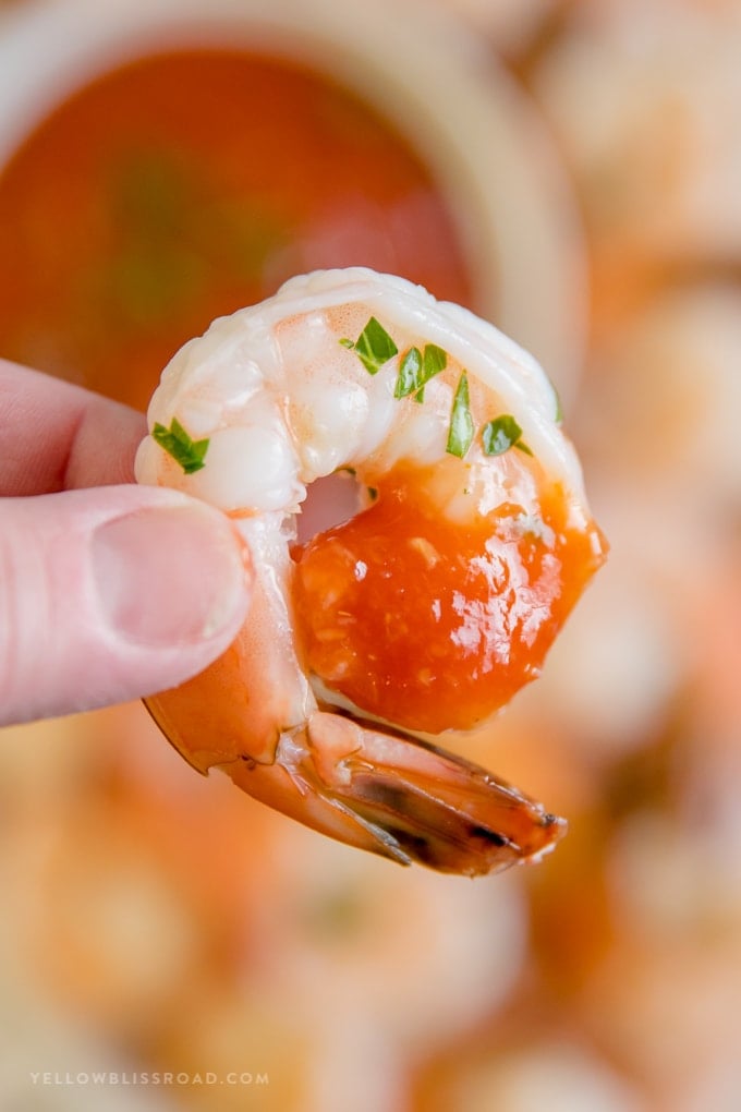 A shrimp dipped in cocktail sauce held betwee two fingers.