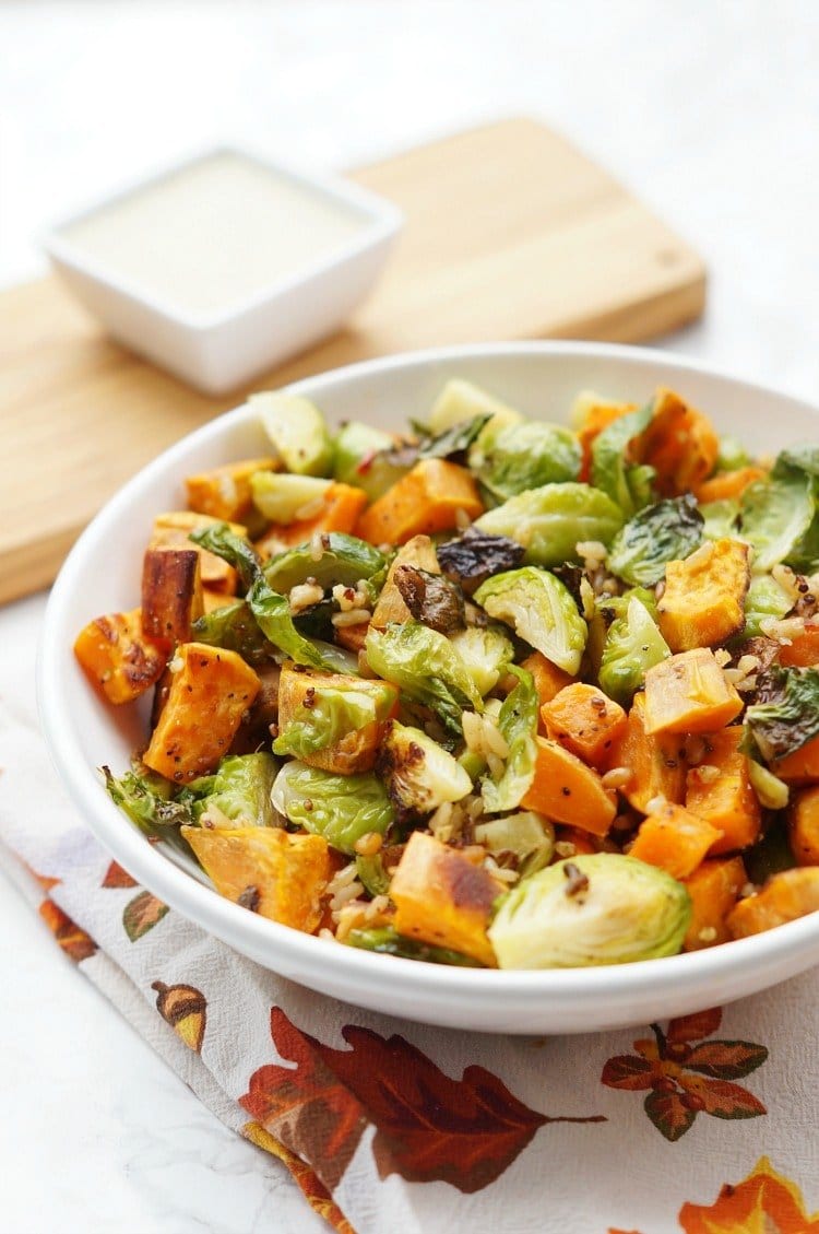 This delicious combination of roasted Brussels sprouts, sweet potatoes, and grains topped with a creamy apple vinaigrette is the perfect Thanksgiving Salad thanksgiving salad in a serving bowl with a ramekin of dressing