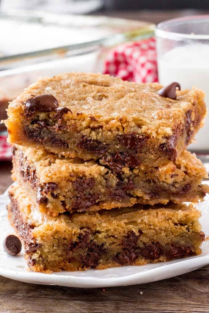A stack of chocolate chip cookie bars with a glass of milk. 