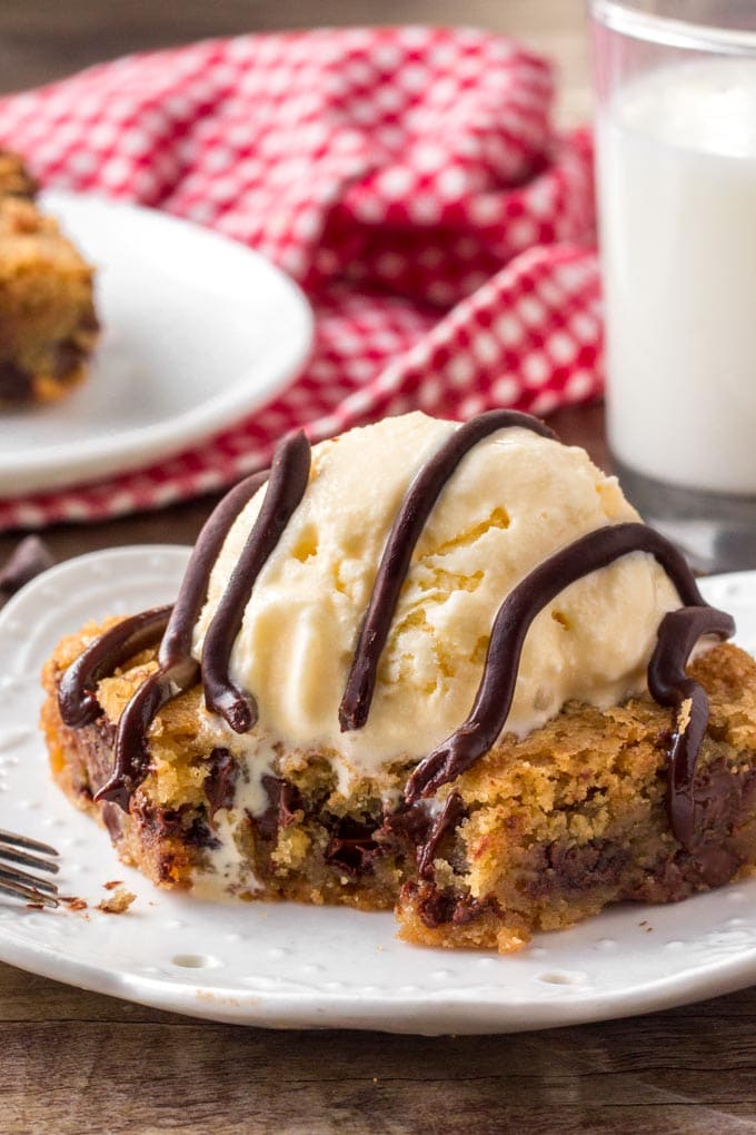 A slice of chocolate chip cookie bars topped with ice cream and chocolate sauce. 