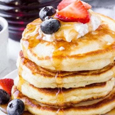 Stack of Greek yogurt pancakes topped with whipped cream, berries & syrup.
