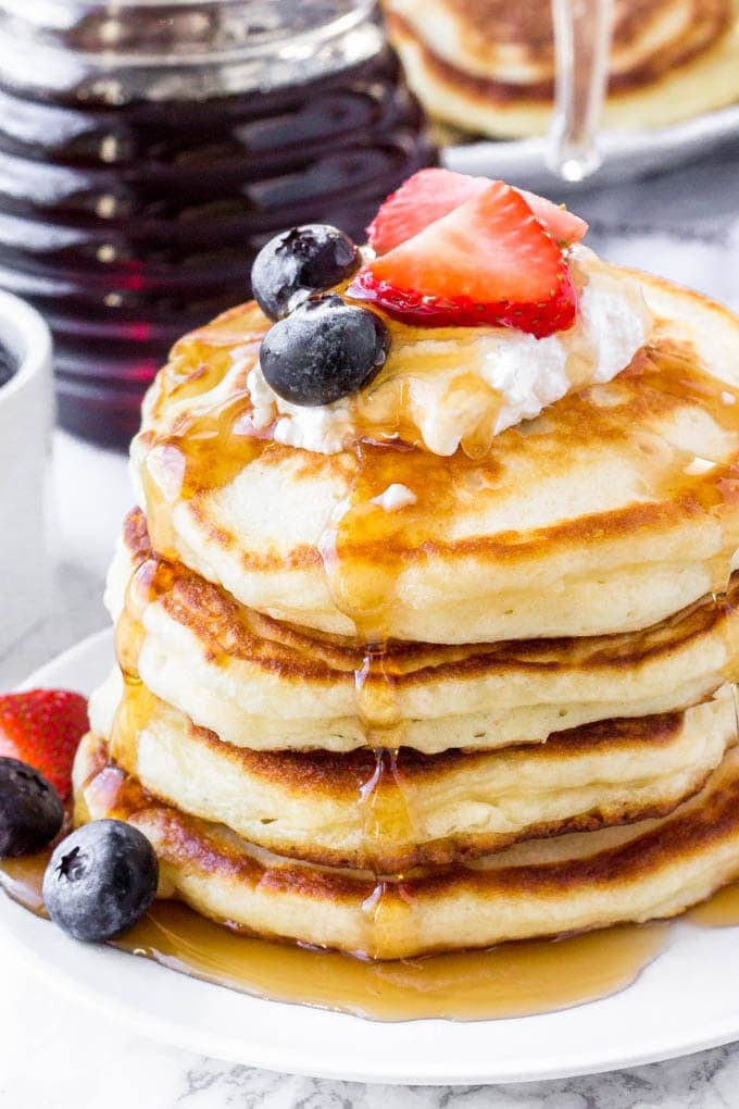 Stack of Greek yogurt pancakes topped with whipped cream, berries & syrup. 