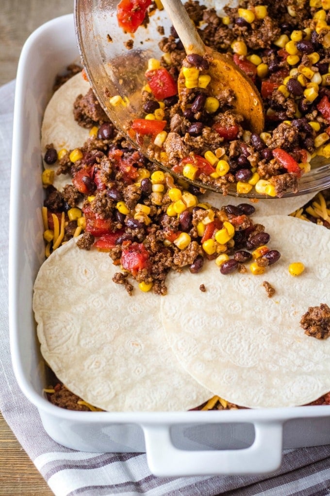 mexican lasagna ingredients being layered in a casserole dish