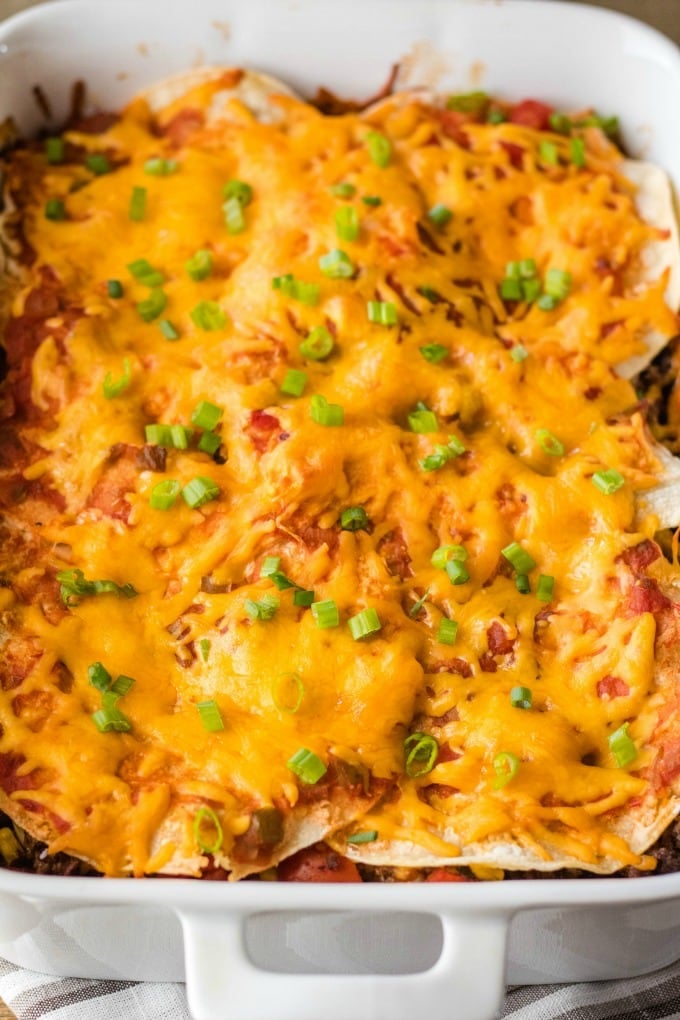 mexican lasagna in a baking dish garnished with green onion