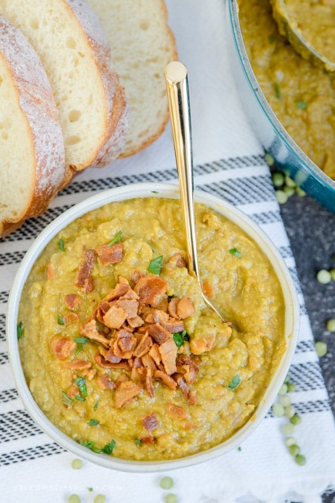 Split Pea Soup Recipe with Bacon in a bowl with a gold spoon and sliced bread on the side.