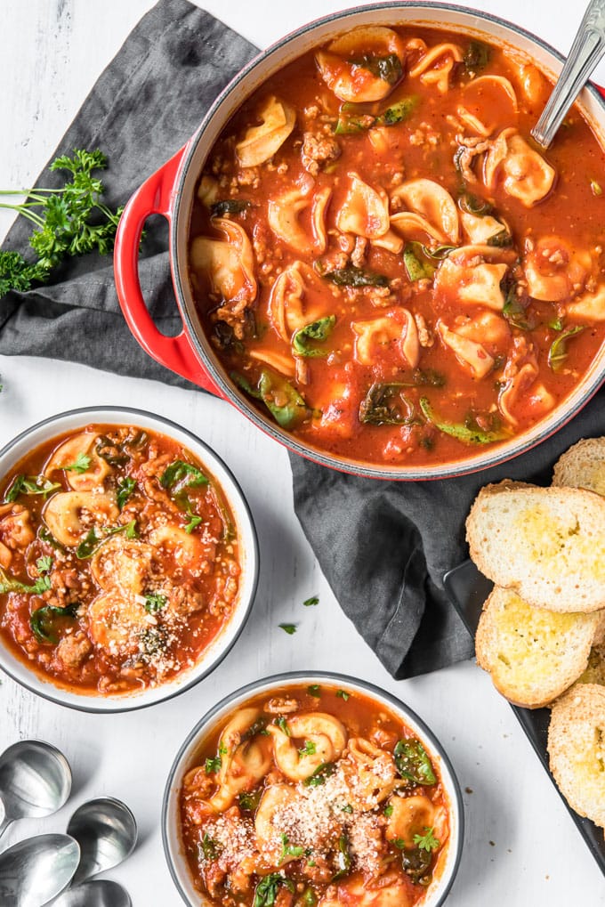 An overhead image of a pot of tortellini soup plus two serving bowls also full of soup