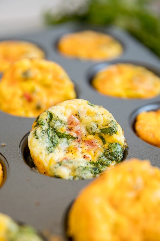A muffin pan full of egg muffins, with a spinach and tomato variety standing up.