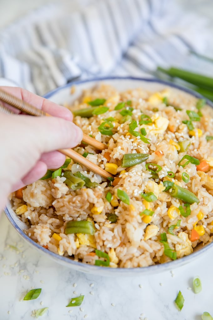 A hand holding chopsticks taking a bite of egg fried rice.