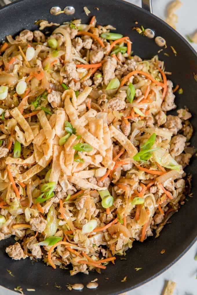 An overhead shot of crack slaw in a large skillet with wonton strips and sliced green onions (egg roll in a bowl).