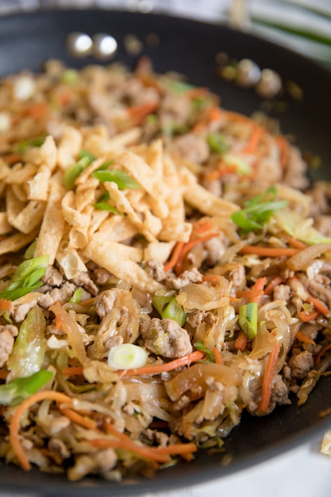 A close up of egg roll in a bowl in a large skillet with wonton strips.